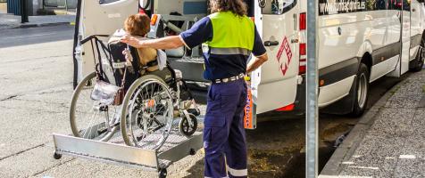Usuario en silla de ruedas subiendo con un elevador a una furgoneta adaptada del servicio de transporte de Fundación Dfa ayudado por un trabajador