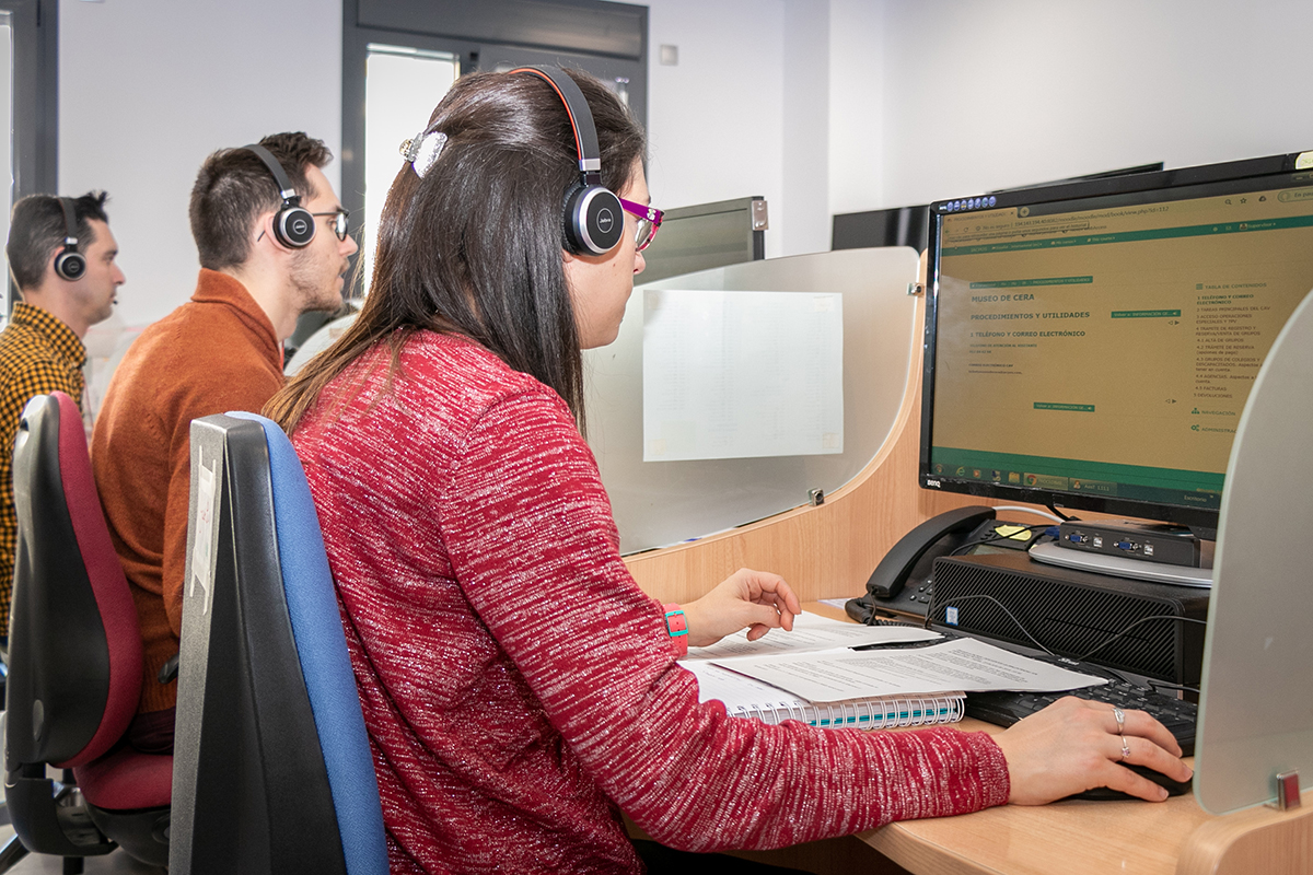 Una mujer y dos hombres trabajando como teleoperadores en una sala de call center