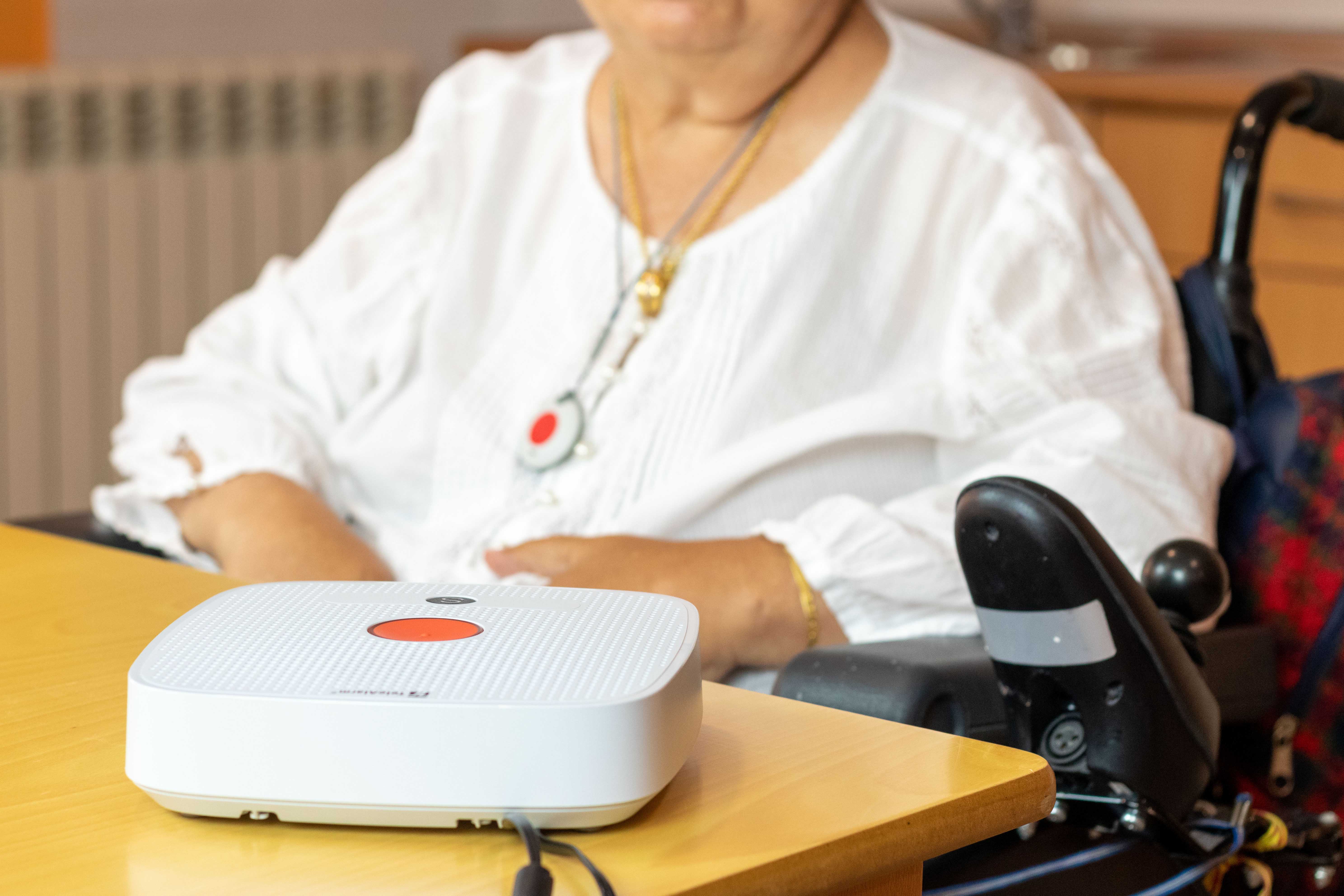 Mujer mayor en silla de ruedas con un botón rojo de teleasistencia