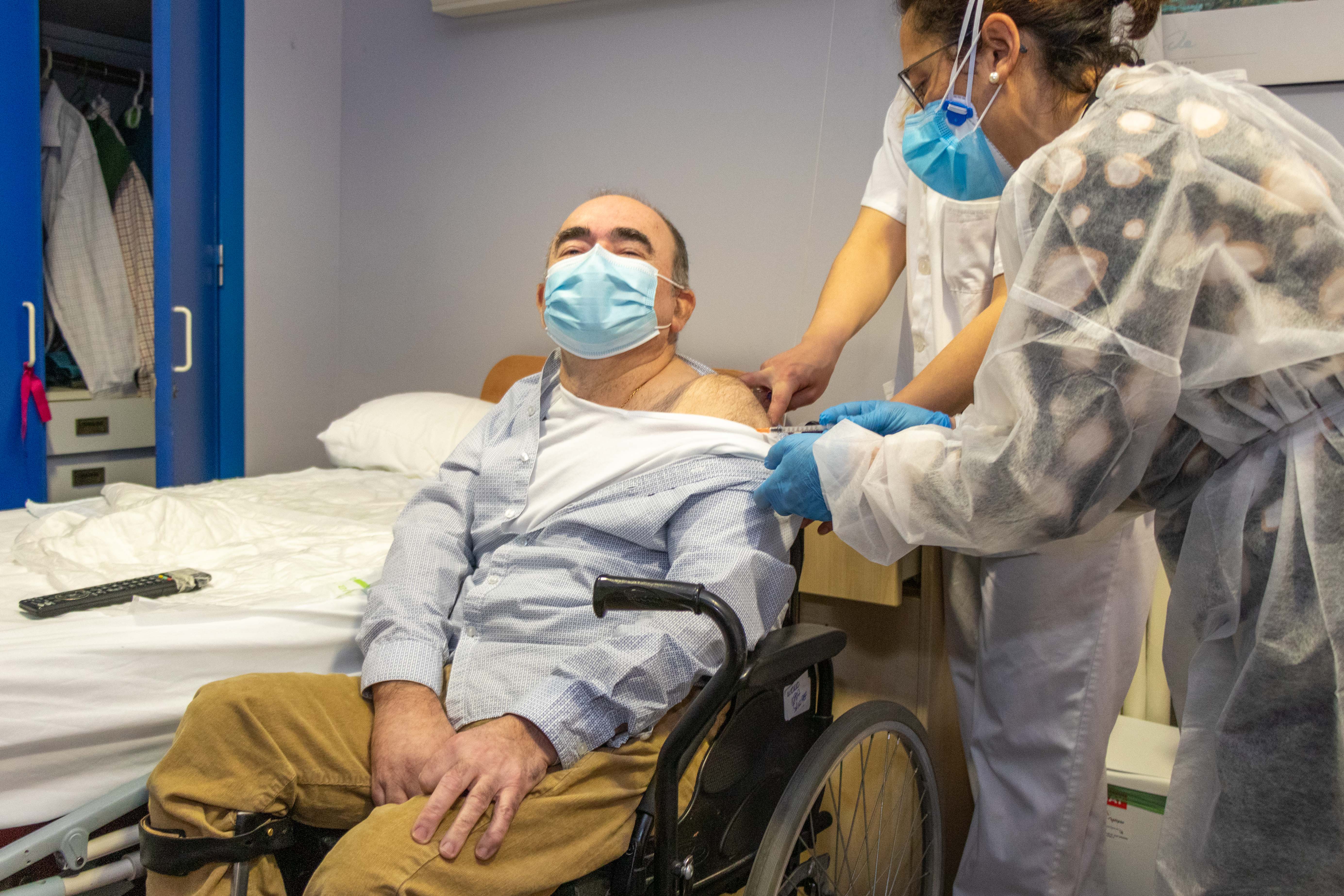 Un hombre en silla de ruedas siendo vacunado por una enfermera equipada con protección frente al covid