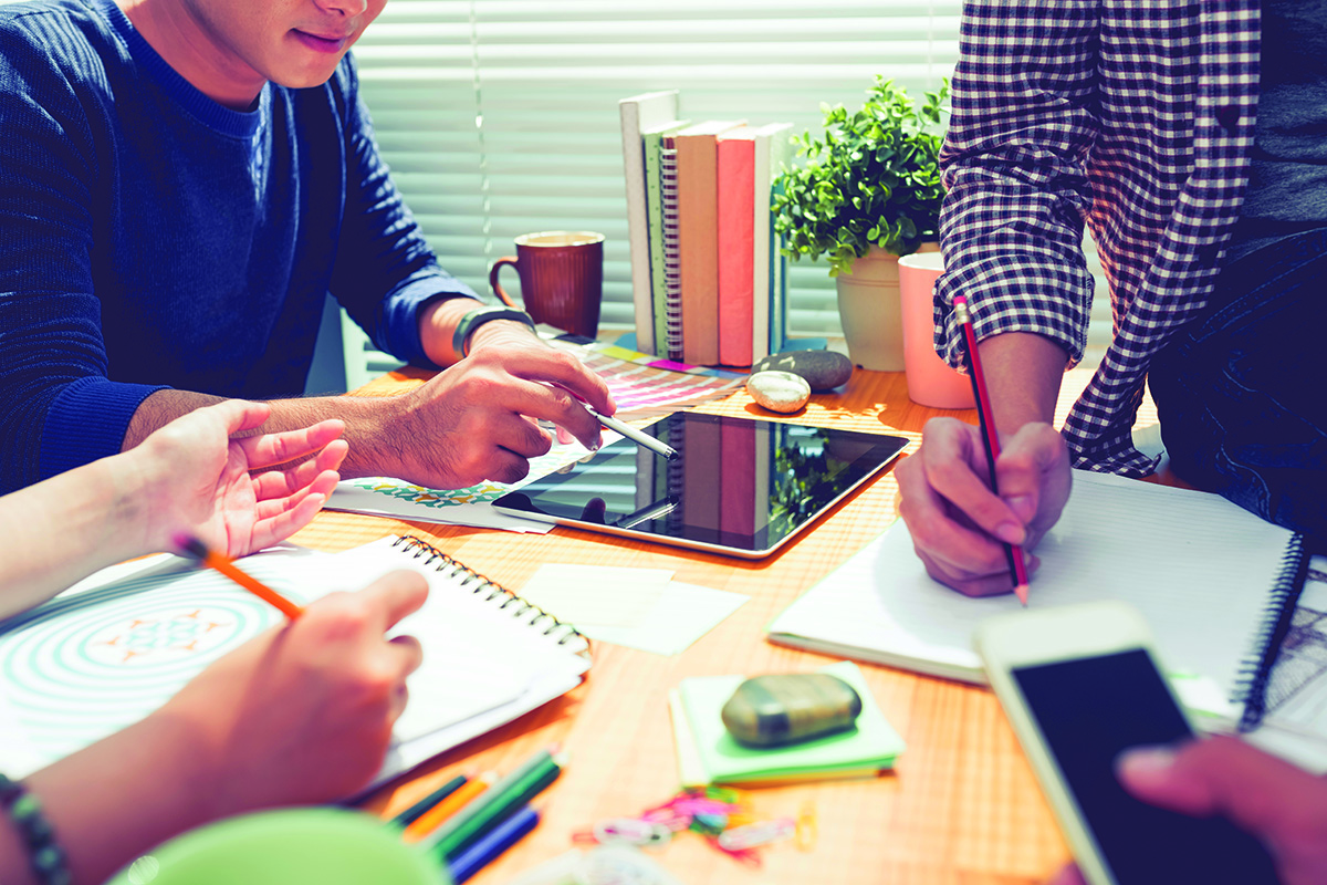 Grupo de personas en una mesa en proceso de búsqueda de empleo escribiendo en cuadernos y tablets