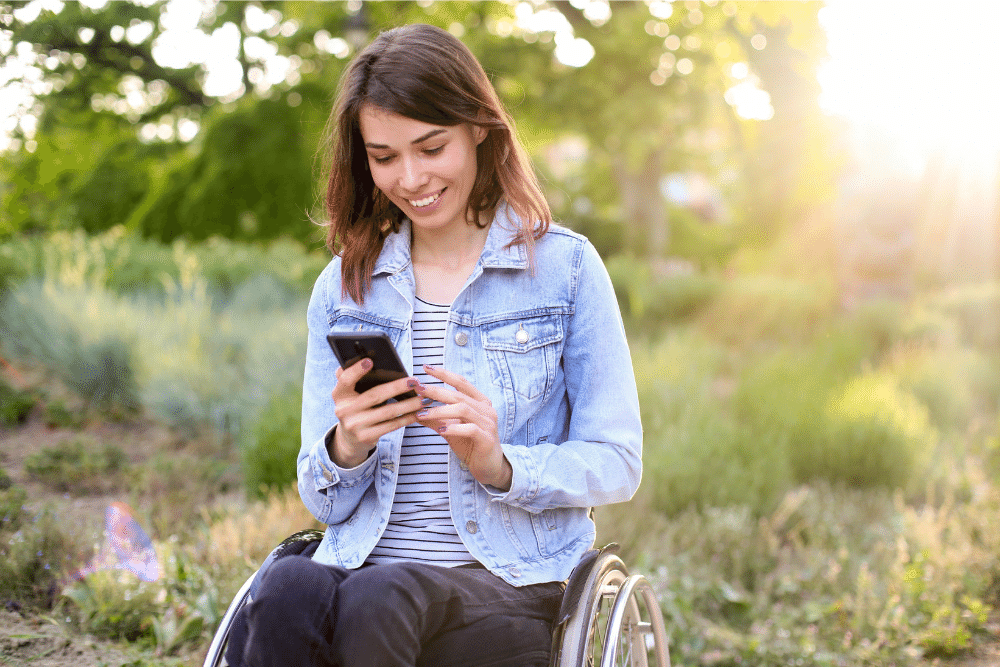 Mujer joven en silla de ruedas con discapacidad usando un móvil en el campo