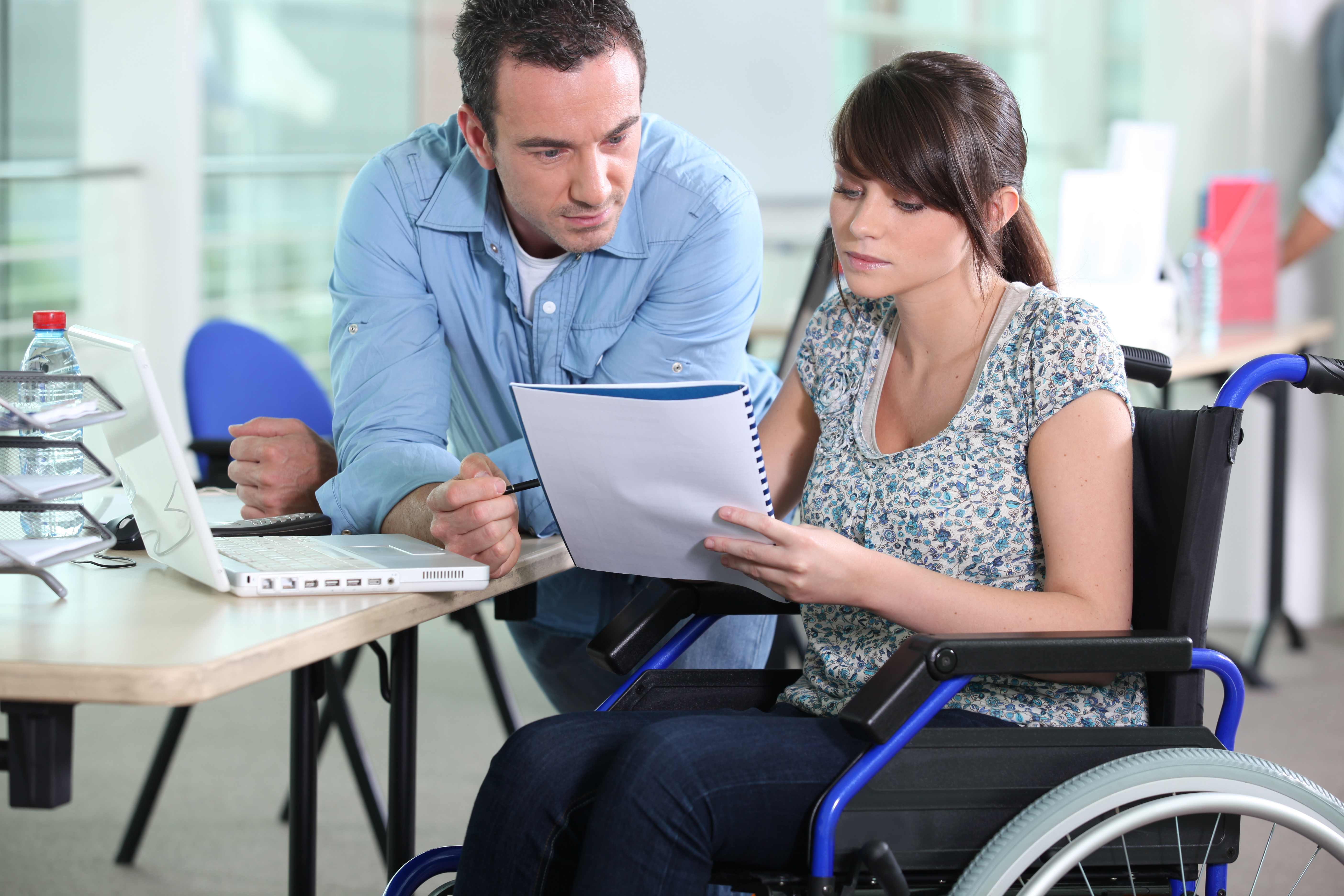 Una mujer en silla de ruedas muestra un cuaderno con información a un hombre