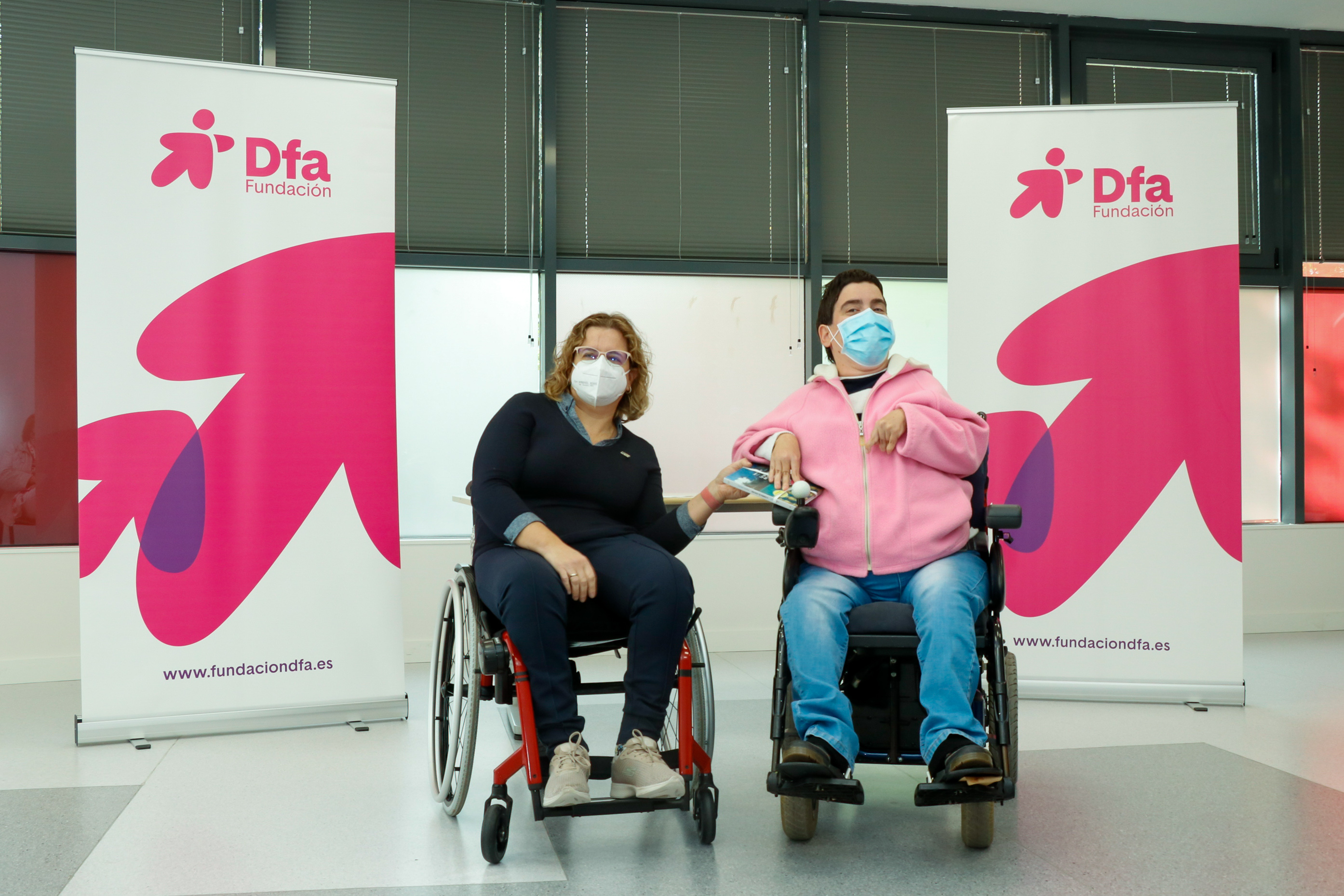 Mujer en silla de ruedas entregando un premio a otra mujer en silla de ruedas