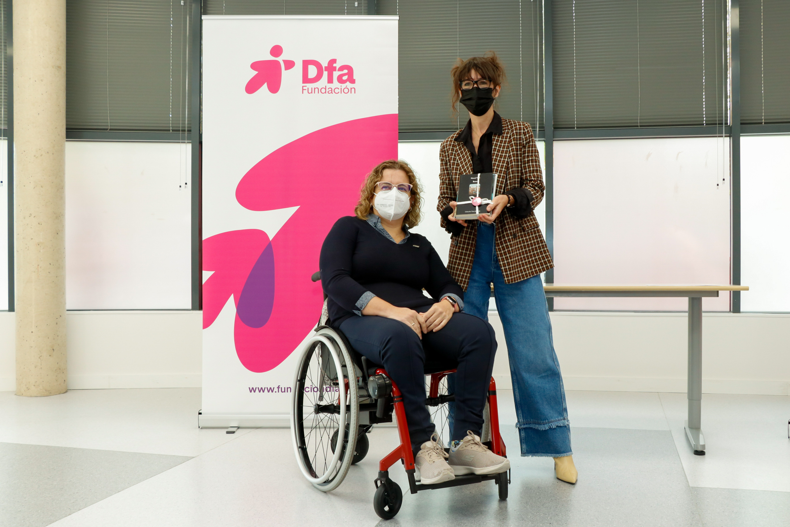 Una mujer posa en la entrega de un premio junto a otra mujer en silla de ruedas