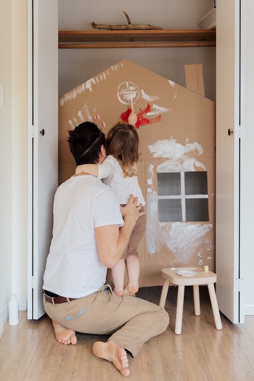 Una niña y su padre junto a una casita de cartón