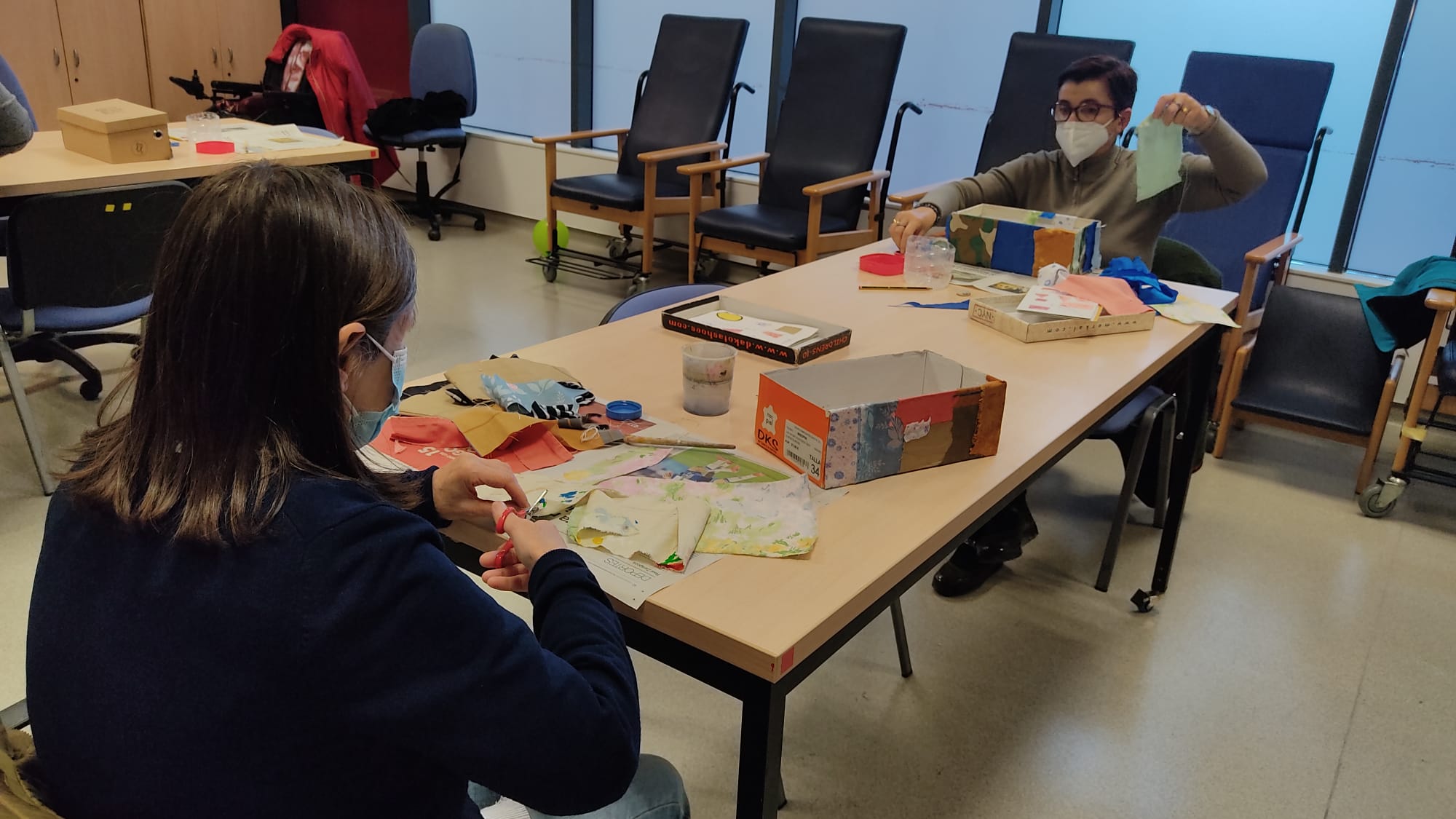 Dos mujeres con discapacidad en una mesa en el taller de costura cortando trozos de telas de colores