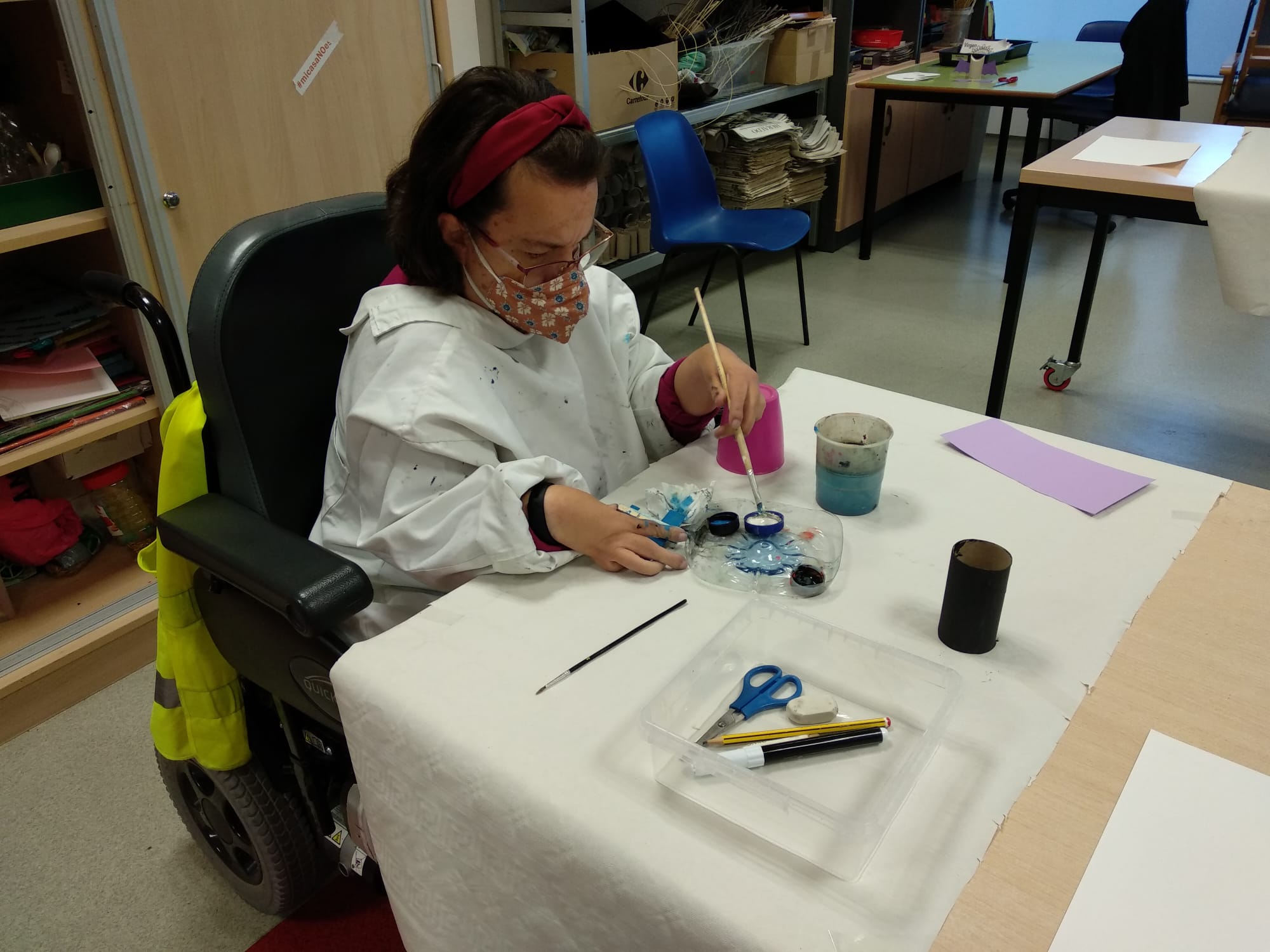 Una mujer en silla de ruedas pintando con pincel en un taller de manualidades