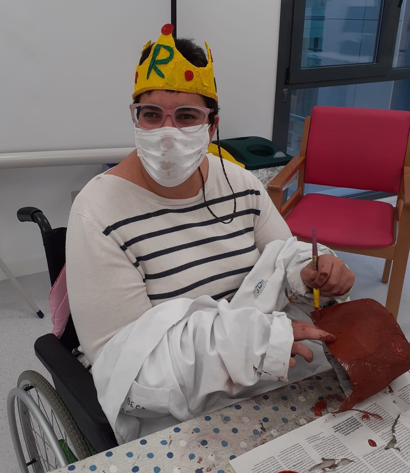 Una mujer con discapacidad muy sonriente con un pincel y una bata realizando manualidades