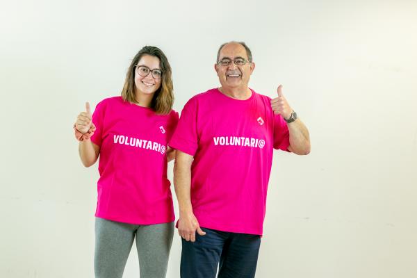 Una chica joven y un hombre, ambos voluntarios, con la camiseta rosa de Dfa