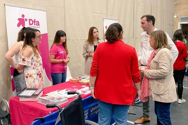 Grupo de personas hablando en un interior cerca de un stand de Dfa