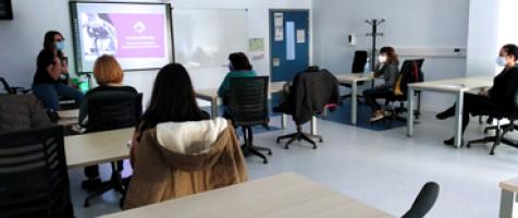 Alumnado en un aula de formación frente a una profesora en una pizarra con una proyección