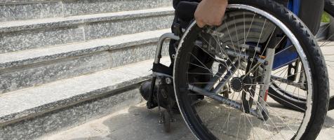 Hombre con discapacidad física en silla de ruedas delante de unas escaleras
