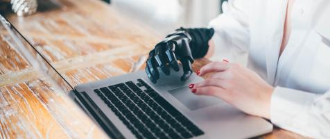 Mujer con mano robótica escribiendo en un portátil encima de una mesa
