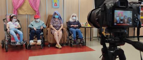 Cámara grabando una actuación teatral de cuatro personas disfrazadas en silla de ruedas