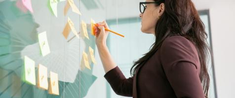 Mujer escribiendo sobre una pizarra transparente llena de posits 