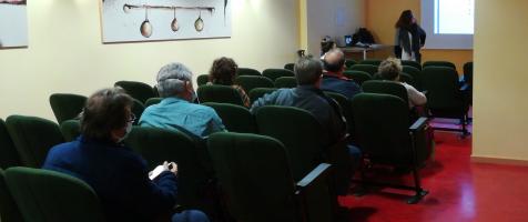 Personas sentadas en butacas en una sala de actos con una mujer dando una charla delante de una proyección