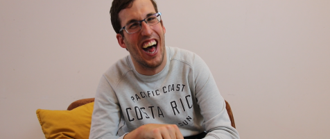 Un joven con discapacidad muy sonriente sentado en un sillón frente a la cámara