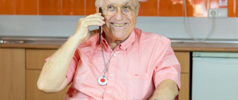 Un señor mayor utilizando el móvil junto a un botón de teleasistencia en el cuello