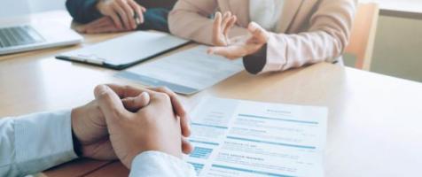 Dos personas sentadas en una mesa con papeles que parecen ser un currículum, trasladando la impresión de ser una entrevista de trabajo