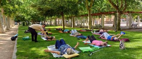 La imagen muestra a las participantes en un Paseo Saludable tumbados sobre un césped y haciendo estiramientos supervisados por un fisioterapeuta de Fundación Dfa 