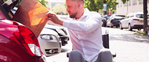 hombre en silla de ruedas metiendo una bolsa de la compra en el maletero del coche