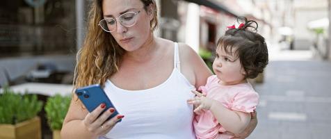 Madre mira el móvil con niña en brazos