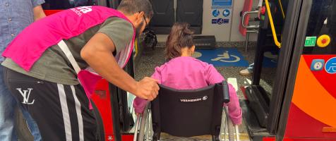 Una persona en silla de ruedas accede a un autobús urbano con el apoyo de un voluntario