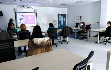 Alumnado en un aula de formación frente a una profesora en una pizarra con una proyección