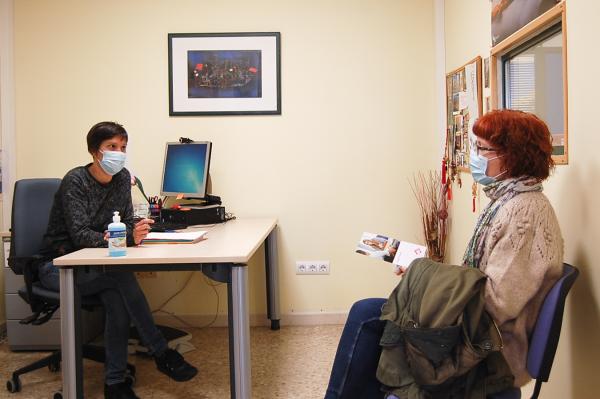 Una trabajadora social en su despacho atendiendo a una usuaria, ambas sentadas y con mascarilla