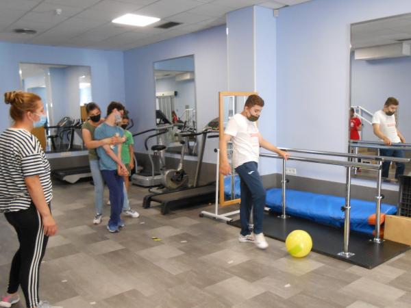 Sala de gimnasio con varios jóvenes con discapacidad y sus acompañantes jugando con un balón