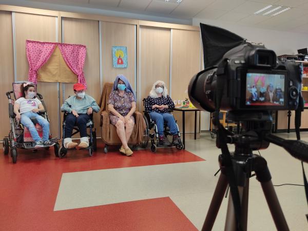 Cámara grabando una actuación teatral de cuatro personas disfrazadas en silla de ruedas