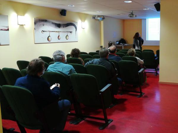 Personas sentadas en butacas en una sala de actos con una mujer dando una charla delante de una proyección