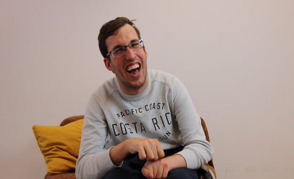 Un joven con discapacidad muy sonriente sentado en un sillón frente a la cámara