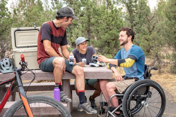 Varios chicos, uno en silla de ruedas, toman un refresco en una mesa al aire libre