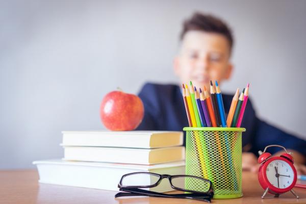 Un alumno aparece en segundo plano rodeado de lápices, libros y unas gafas