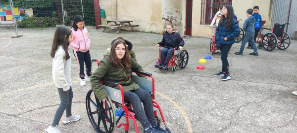 Unos niños montados en sillas de ruedas en el patio del colegio