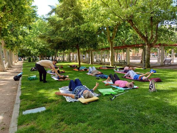 La imagen muestra a las participantes en un Paseo Saludable tumbados sobre un césped y haciendo estiramientos supervisados por un fisioterapeuta de Fundación Dfa 