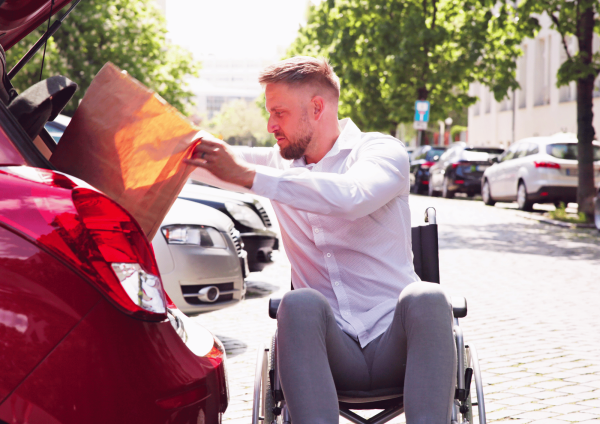 hombre en silla de ruedas metiendo una bolsa de la compra en el maletero del coche
