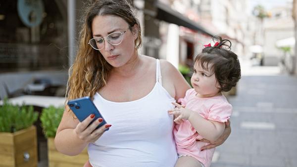 Madre mira el móvil con niña en brazos