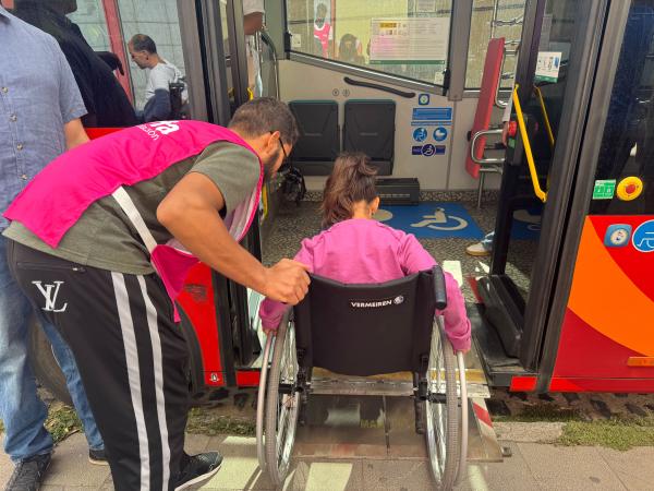 Una persona en silla de ruedas accede a un autobús urbano con el apoyo de un voluntario