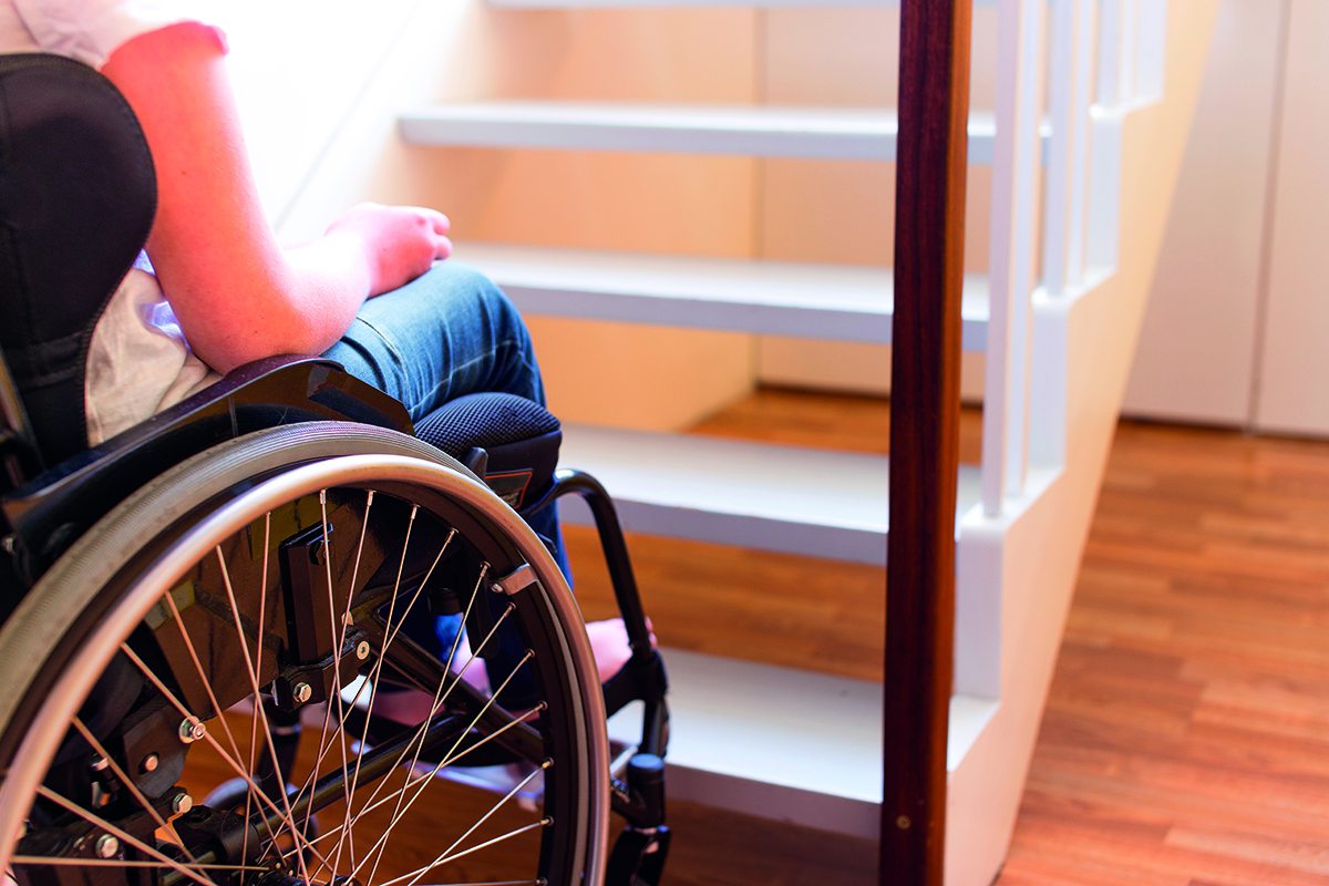 Mujer en silla de ruedas delante de unas escaleras en una casa