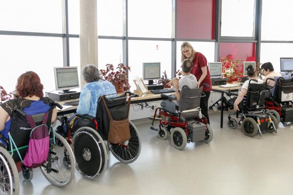 Sala de ordenadores con varias personas en silla de ruedas utilizándolos